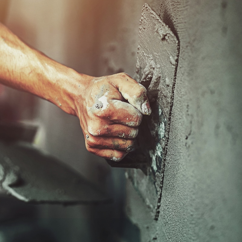 Main d'un ouvrier appliquant du ciment frais sur un mur avec une truelle, le plâtre couvre la main sale.