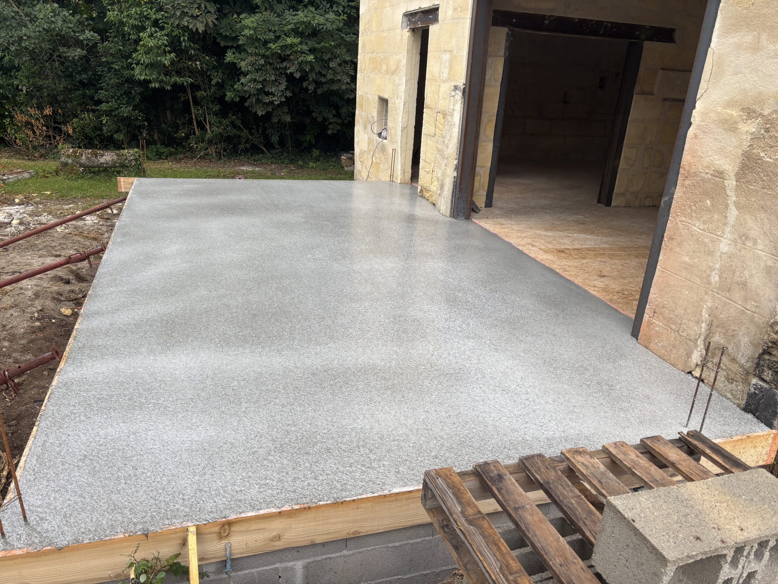 Dalle de béton fraîchement coulée et lissée pour une terrasse de maison en pierre en cours de rénovation.