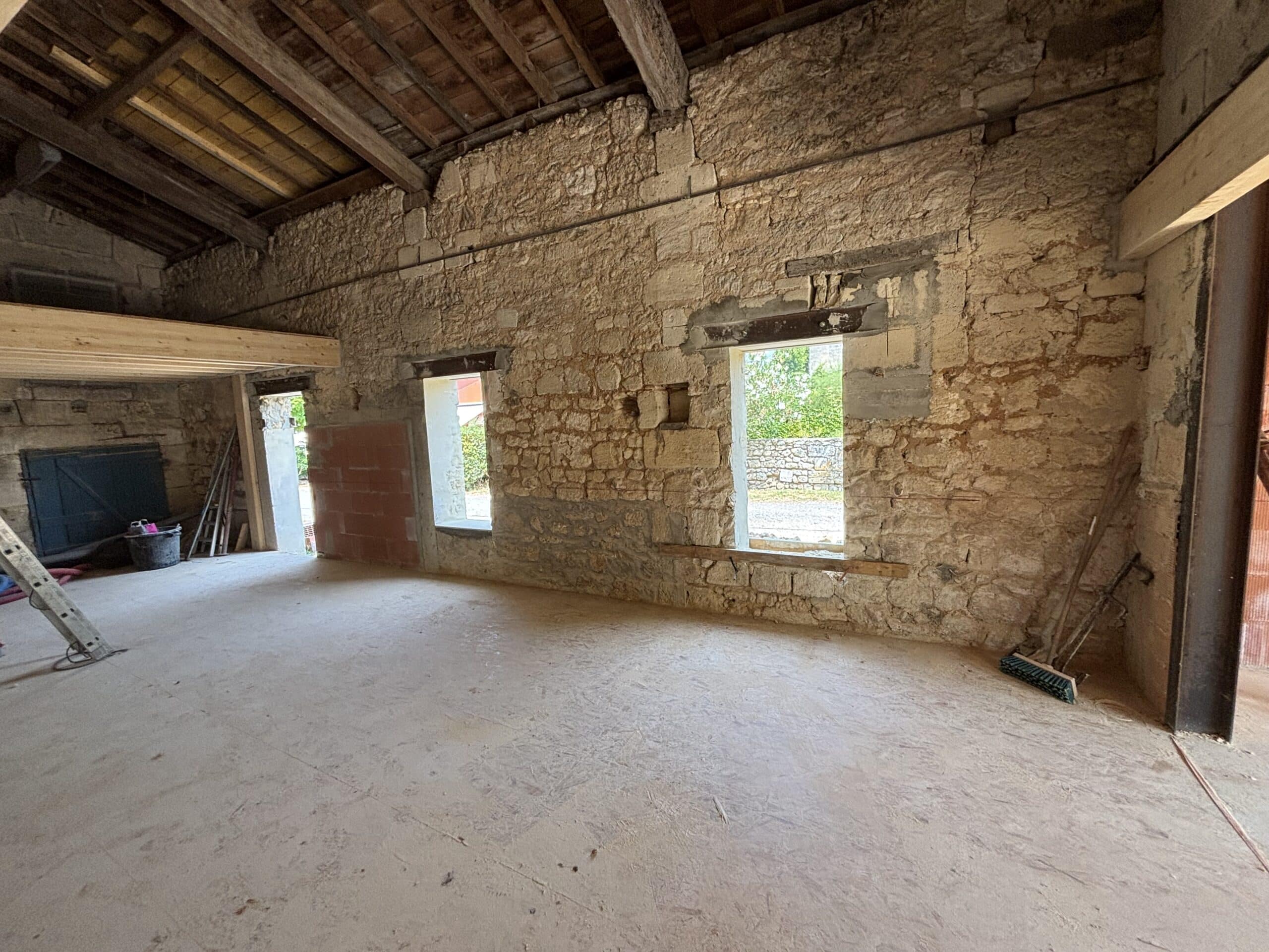 Chantier de rénovation d'une grange avec murs en pierre apparente, charpente en bois et mezzanine neuve.