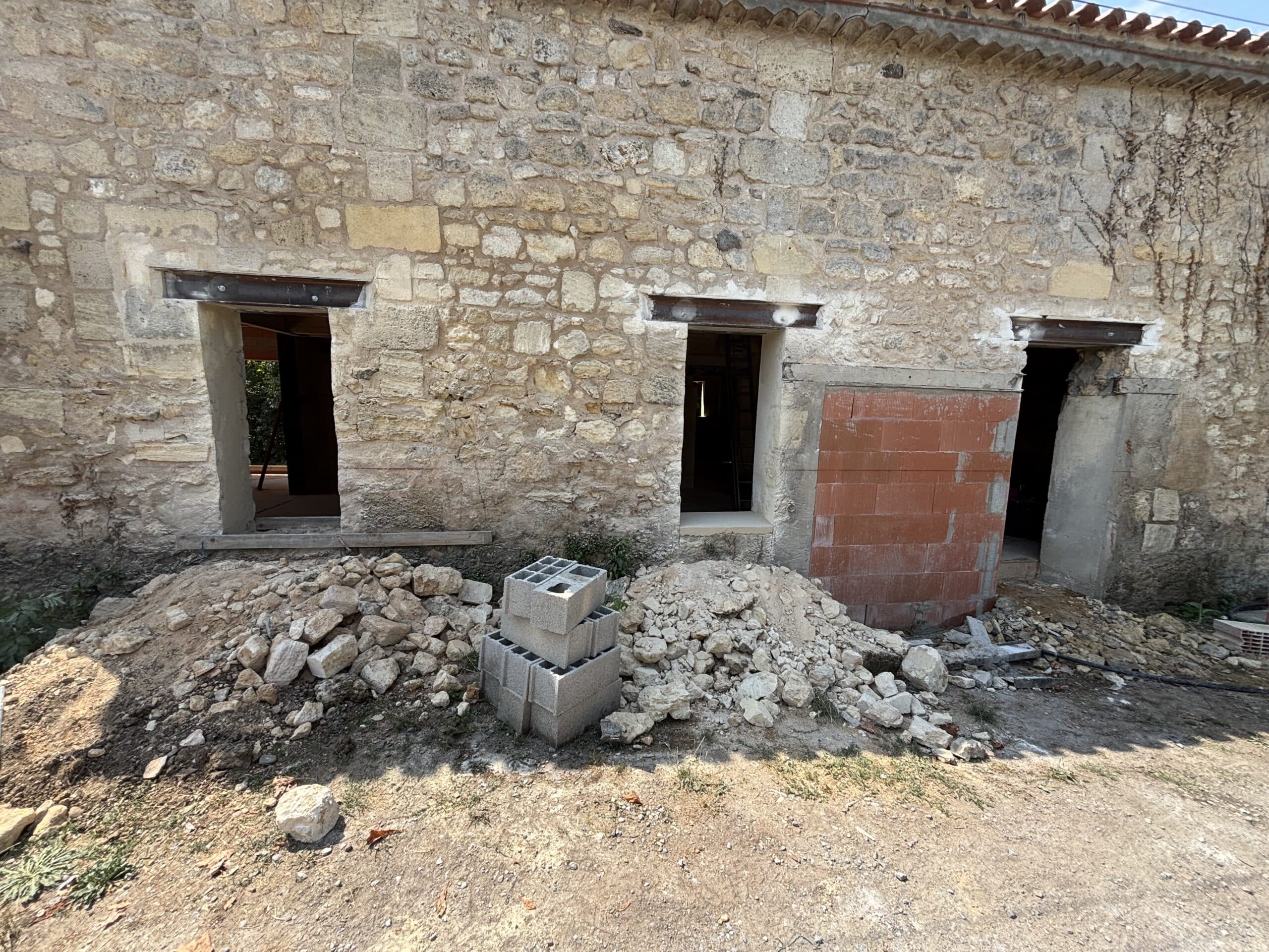 Rénovation d'une maison en pierre avec linteaux en acier, ouvertures et tas de gravats au sol.